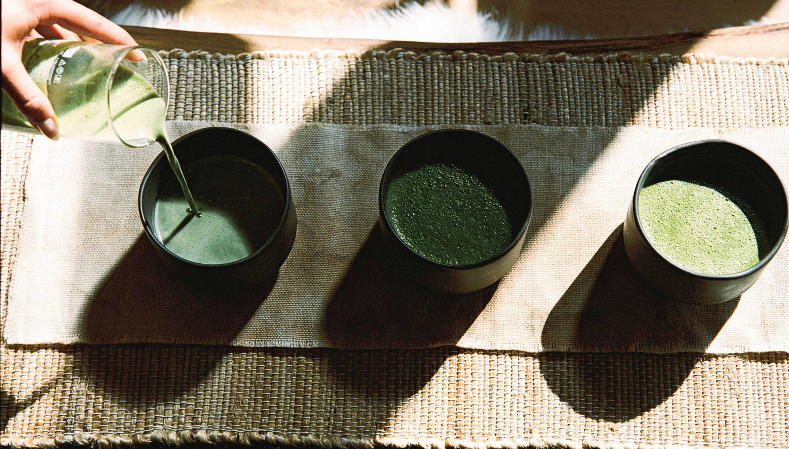 Bowl of whisked Ascend matcha latte beside the matcha tin and a bamboo whisk